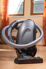 The Vacuum Cleaner on a laminate floor at room with windows on background. Cleaning the wooden floors with hoover, close up view.