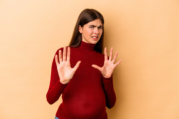 Young caucasian pregnant woman isolated on beige background rejecting someone showing a gesture of...