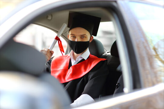 the graduate student in graduation gown and a square cap and a face mask sits in the car before the start of the ceremony