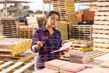 Concentrated hispanic woman worker controlling quantity of tiles at hardware store warehouse