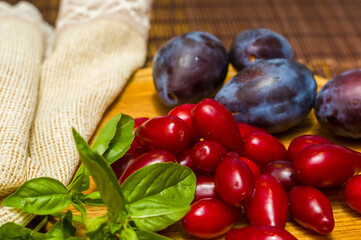 Still life - fresh large dogwood berries, purple plums and a sprig of basil on a wooden board