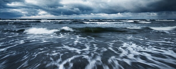 Storm clouds above the Baltic sea in winter, long exposure. Dramatic sunset sky, waves and water splashes. Dark seascape. Germany