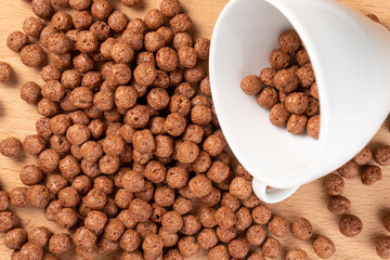 Chocolate cereal balls are scattered over the board with a white teacup