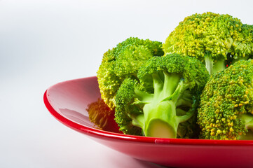 Sliced raw fresh head of broccoli cabbage in a red plate on white background, healthy vegetarian food, close-up