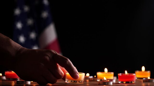 Memorial Day, Man hand put a burning candle on wooden table for honoring and mourning with American flag background. Concept of Memorial Day or 4th of July,Independence Day,Veterans Day, USA flag.