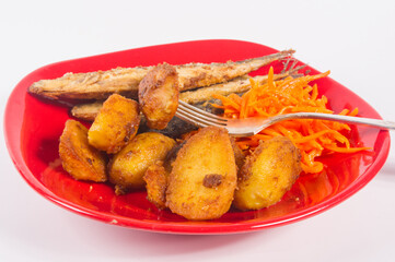 Homemade dish - fried potato wedges with small fish and pickled carrots on a red plate, simple rustic food, close-up.