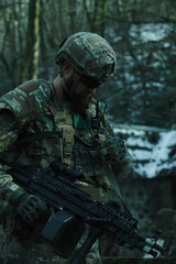 Fototapeta premium Portrait of airsoft player in professional equipment with machine gun in the forest. Soldier with weapons at war