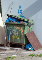 Duży zielony kosz na śmieci pomalowany farbą w sprayu. Tekst graffiti. - obrazy, fototapety, plakaty