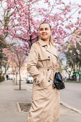 Beautiful woman near sakura trees. Pink flowers bloom in the trees on a city street. Trees bloom around. Spring time concept