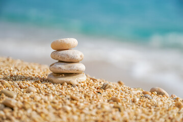 Fototapeta na wymiar Stones balancing on sea beach. Pyramid of pebbles on sandy shore. Stable pile or heap in soft focus with bokeh, close up. Zen balance, minimalism, harmony and peace