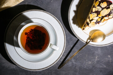Still life - layered homemade sponge cake and a cup of black tea in a white dish, and a linen napkin, black background, hard light, photo in a low key.
