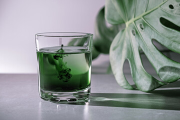 Chlorophyll extract is poured in pure water in glass against a white grey background with green leaf. Liquid chlorophyll in a glass of water. Concept of superfood, healthy eating, detox and diet - obrazy, fototapety, plakaty