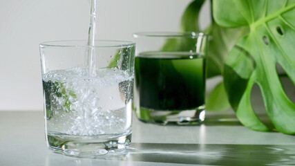 Chlorophyll extract is poured in pure water in glass against a white grey background with green...