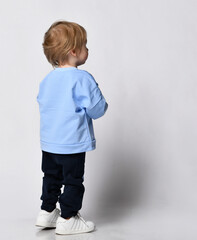 Rear view of a boy in a blue sweatshirt walking towards free copy space against a gray wall. Happy...