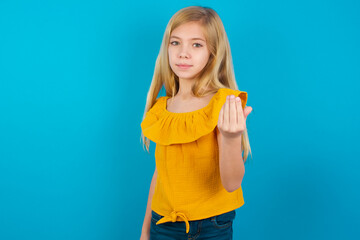 Caucasian kid girl wearing yellow T-shirt against blue wall inviting to come with hand. Happy that you came