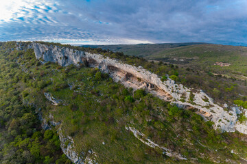 Fototapeta na wymiar Aerial drone view of Veli Badin, natural stone cliff carved in the rock overlapping the ground, during a sunny afternoon. Majestic rock structure in slovenian Karst.