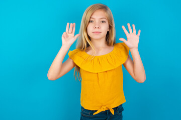 Caucasian kid girl wearing yellow T-shirt against blue wall showing and pointing up with fingers number nine while smiling confident and happy.