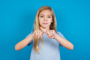 beautiful Caucasian little girl wearing blue T-shirt over blue background has rejection angry...