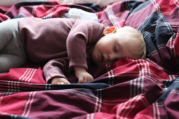 Little cute girl sleeps on plaid bedding. Daytime sleep of a baby
