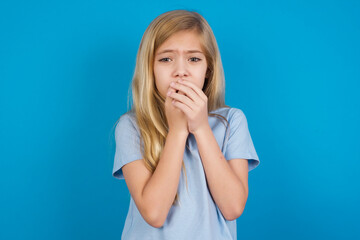 Sad beautiful Caucasian little girl wearing blue T-shirt over blue background feeling upset while spending time at home alone staring at camera with unhappy or regretful look.