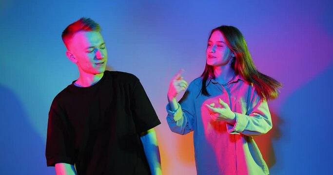 Cool modern young teen couple guy and girl dancing, laughing, talking and flirting in colourful neon studio light