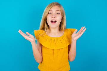 Surprised terrified Caucasian kid girl wearing yellow T-shirt Gestures with uncertainty, stares at...
