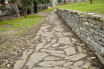 Cobblestone way and path in Gulhane public park with white street lamps and withered and dried trees and green grass during overcast sky and rain and bosporus background.