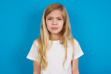 Offended dissatisfied beautiful Caucasian little girl wearing white T-shirt over blue background with moody displeased expression at camera being disappointed by something