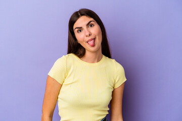 Young caucasian woman isolated on purple background funny and friendly sticking out tongue.
