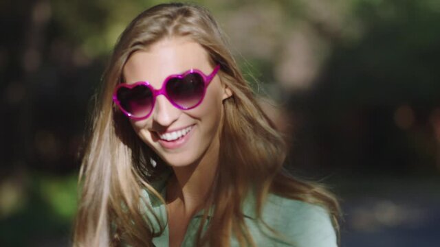 Portrait of a girl standing outside looking into camera and putting on heart shaped sunglasses.
