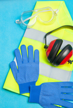 
Vista de diversos elementos de protecci&oacute;n para la seguridad en el trabajo como gafas, chaleco reflectante, cascos de protecci&oacute;n auditiva y guantes sobre un fondo azul