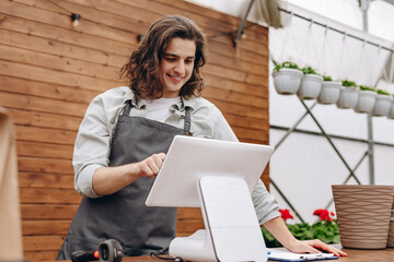 Attractive male florist and standing near cash register, waiting for clients in flower shop.