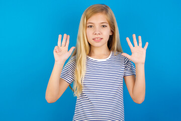 Caucasian kid girl wearing striped shirt ​against blue wall  showing and pointing up with fingers number nine while smiling confident and happy.