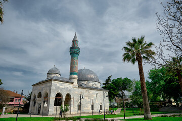Fototapeta na wymiar Bursa, Turkey. Green mosque (yesil camii) in Nicaea (iznik) during spring and sunny day in center of the city covered by many green plants, and palm trees and it turquoise color minaret