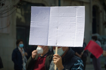Homem no meio de uma multidão numa manifestação a segurar um cartaz, em tempo de pandemia de...
