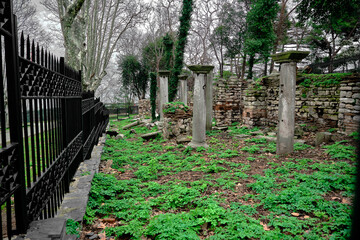 Naklejka premium Old remainings and ruins from byzantium in covered by metal and black fences. There are many green plants and greens around the roman ruins in istanbul gulhane park during overcast and rainy day.