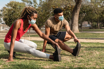 Multiracial people doing stretching routine outdoor at city park wearing safety masks - African friends and workout sport exercises concept - Focus on man face