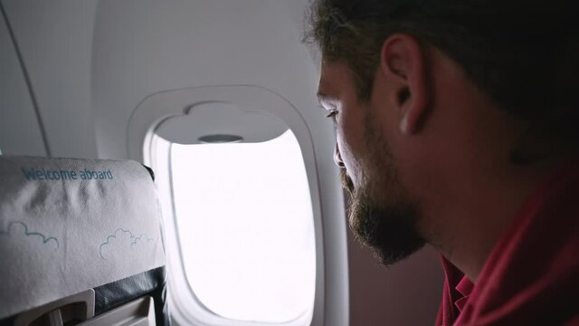 Side view of a man looking through a plane window. Handsome male traveler on an air journey. High quality 4k footage