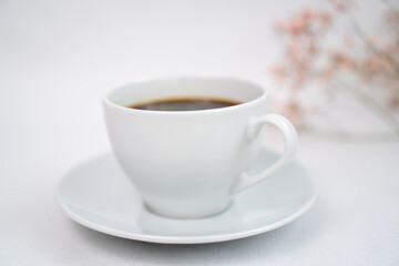a cup of black coffee on a white table and with a sprig of dried flowers