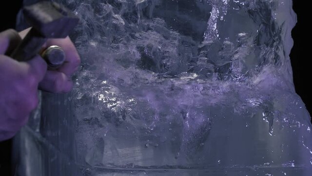 Artist is creating an ice sculpture by using chisel and hammer on a block of ice