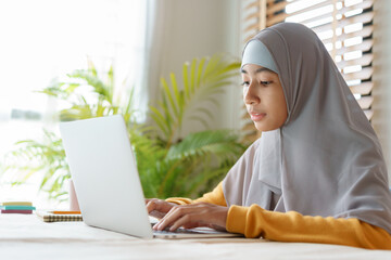  Muslim student girl wear hijab typing work on computer laptop at home - 431816521