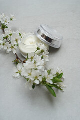 Beauty cream in a glass jar on a light gray background. Decorated with white spring flowers. Unbranded skincare product. Cosmetic cream. Close up, selective focus, high angle. . - 431817749