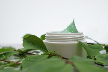 Beauty cream decorated with green leaves. Unbranded skincare product. Green cosmetic cream. Close up, selective focus, side view. - 431817755