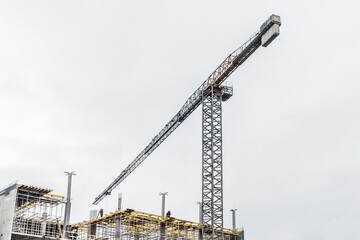 Fototapeta na wymiar Industrial tower crane builds new concrete city building or apartments on construction site