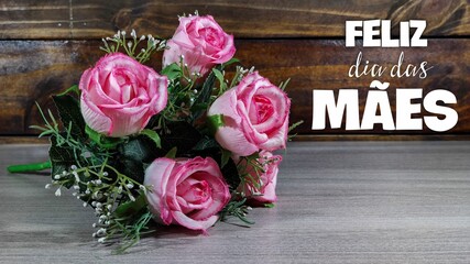 Mother's day card with Portuguese words: Happy Mothers day, pink roses on wood background.