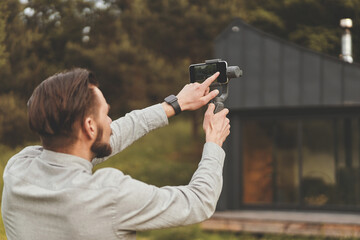 Back view of millennial man recording video at smartphone with tripod