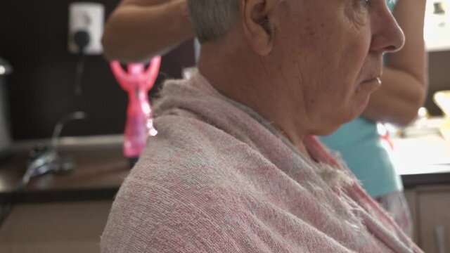 Close up head profile of house bound senior grey haired man having haircut in home kitchen. Copy space.