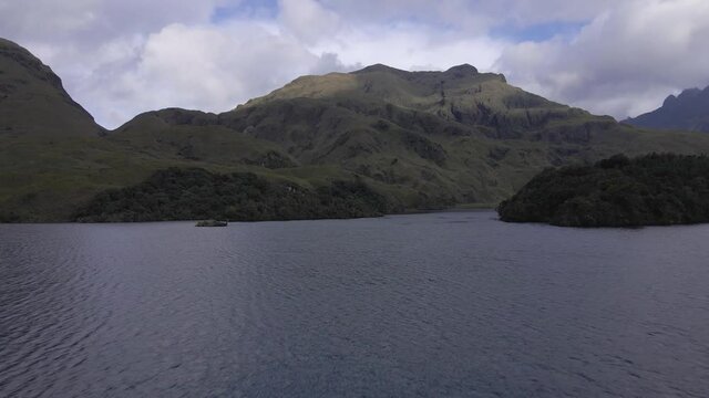 Aerial flyover tranquil Atillo Lagoons with green mountains in background during cloudy day. Chimborazo province,Ecuador.