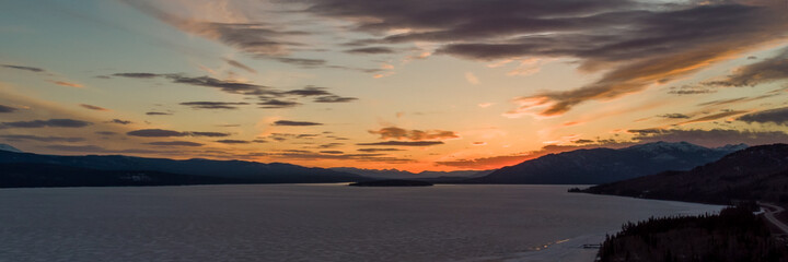 Panoramic view of a northern Canadian sunset in April with bright orange hues. From a frozen lake in spring time with blue sky and clouds rolling across the sky. 