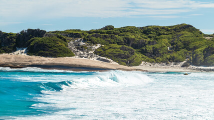 Naklejka premium Landscape view of waves breaking over smooth granie rocks at Blue Haven Beach near Esperance in Western Australia under a bright clear blue sky.